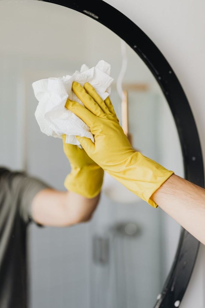 Gloved hand wiping a round bathroom mirror with a paper towel