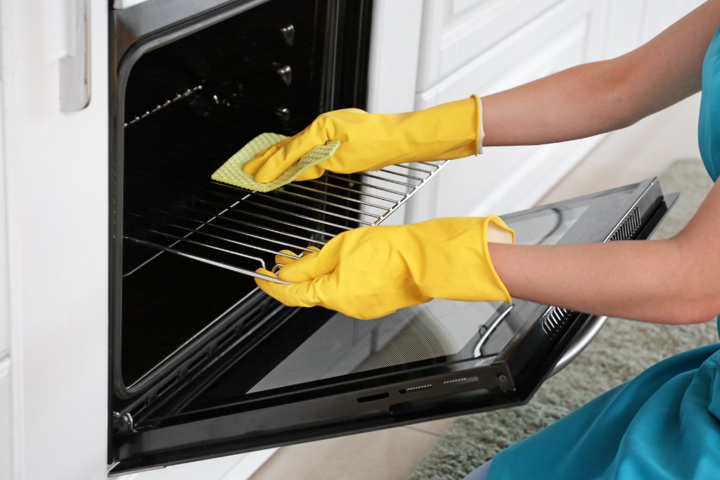 Gloved hands scrubbing an oven rack with a green sponge